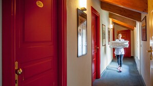 A hallway with red doors, a number sign, and a person carrying a large item. - Phi Hotel Palio (Asti)