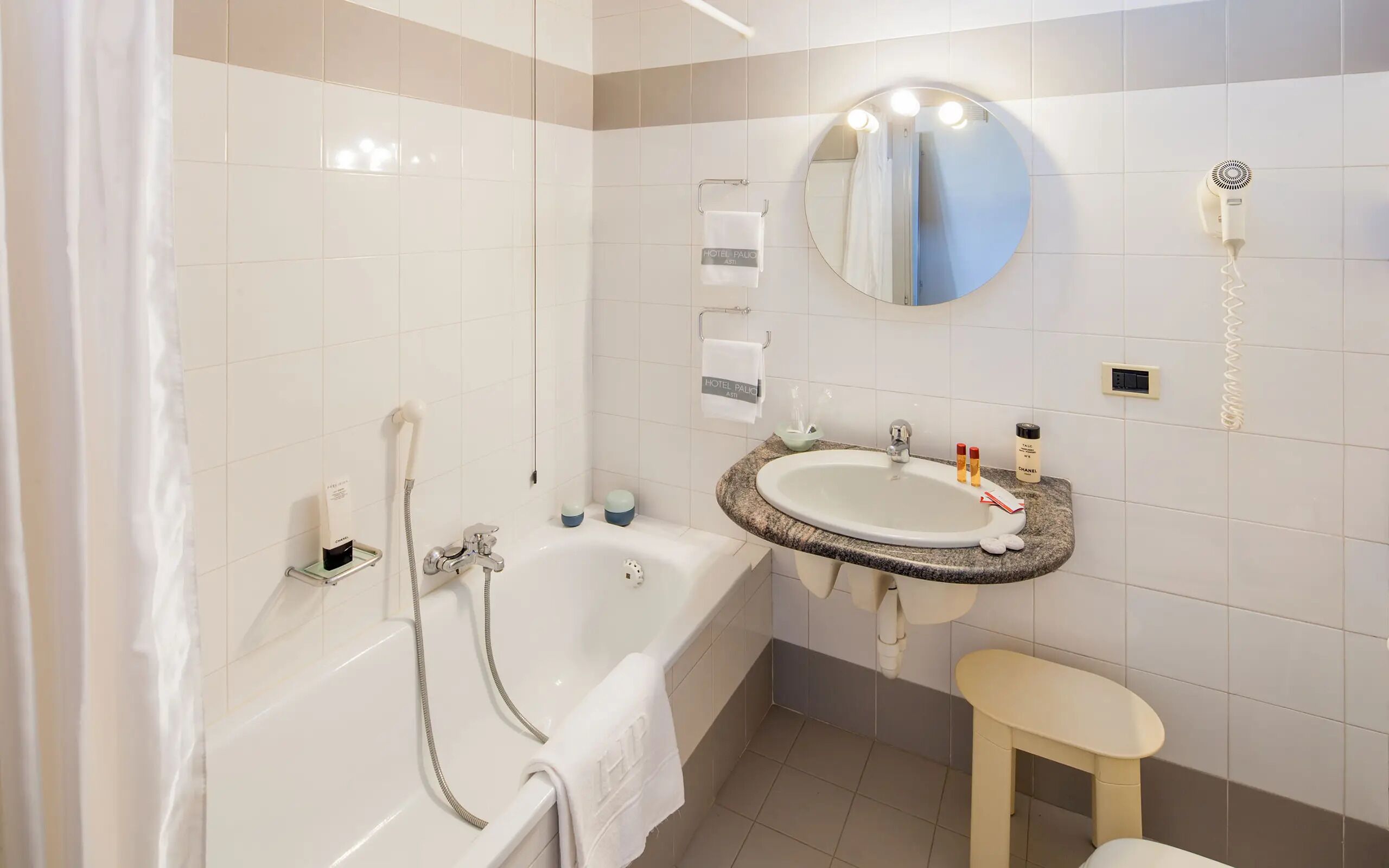 A bathroom with a bathtub, a sink, a mirror, a hairdryer, and a towel rack.