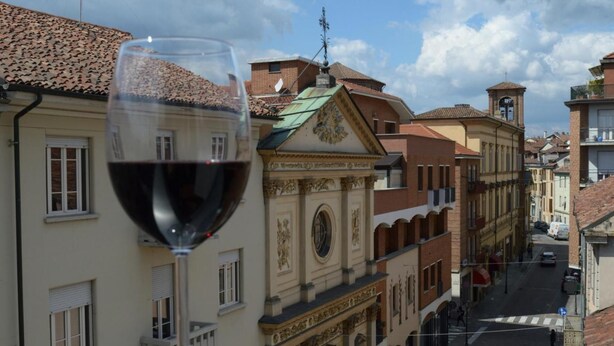 A view of a street with buildings and a glass of red wine on a table. - Phi Hotel Palio (Asti)
