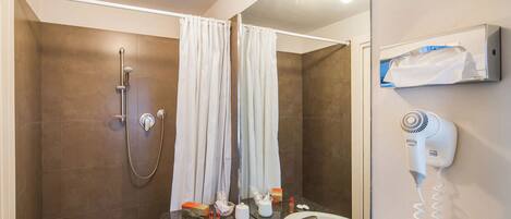 Un baño con ducha, dos lavamanos, un secador de pelo y un perchero para toallas.