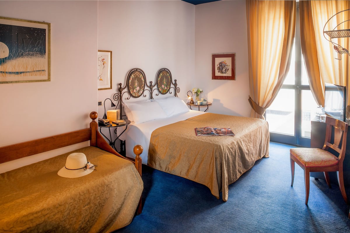 A hotel room with two single beds, a wooden chair, a small table with a lamp, and a TV.