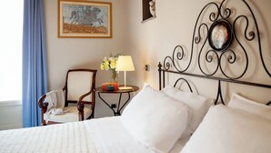 A neatly made bed with white linens, a wooden chair, a small table with a lamp and flowers, and a framed artwork on the wall. - Phi Hotel Palio (Asti)