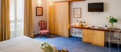 Habitación de hotel con cama, escritorio, silla, armario, televisión y ventana con cortinas.