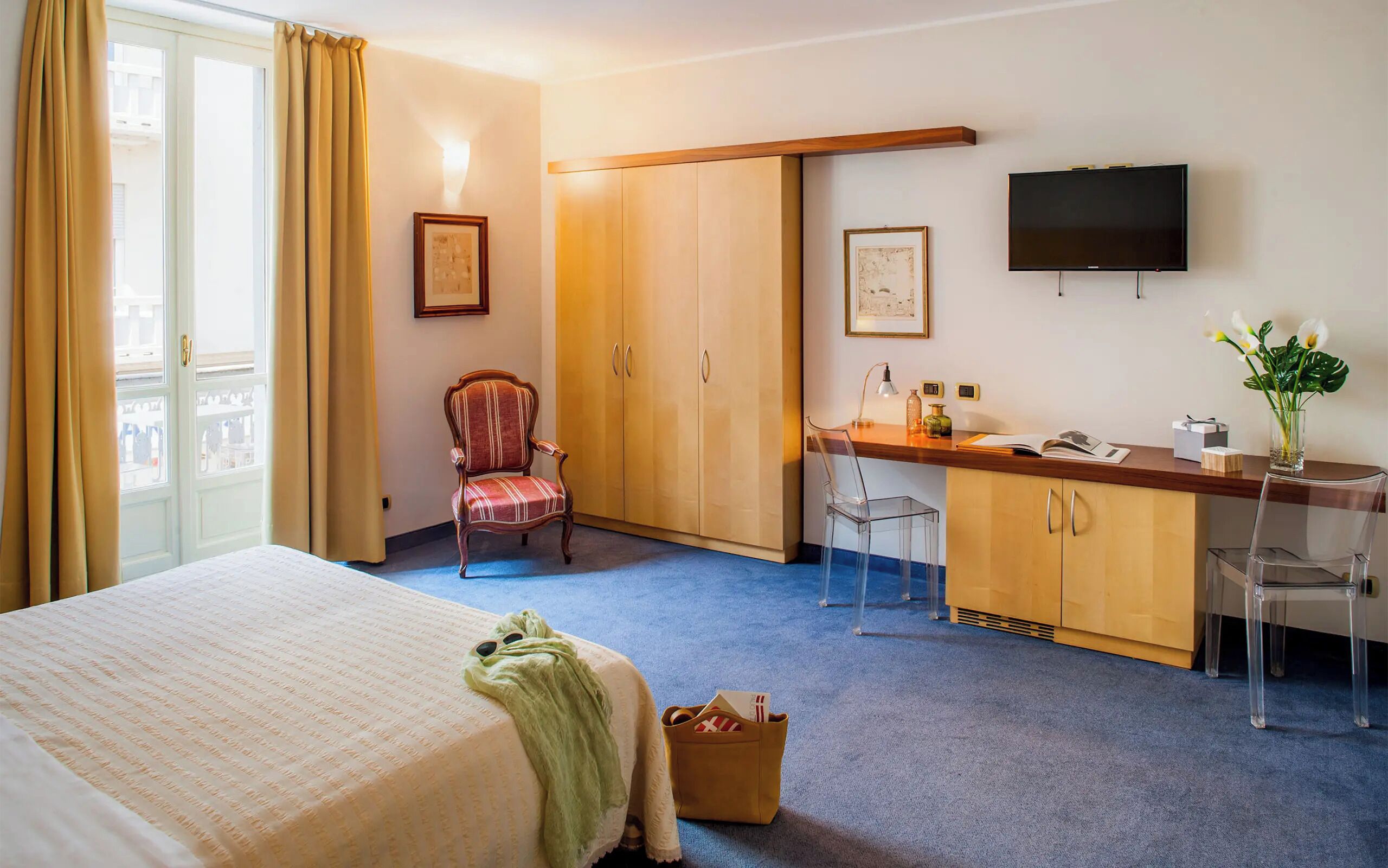 Une chambre d’hôtel comprenant un lit, un bureau avec une chaise, une armoire, une télévision et une fenêtre avec des rideaux.