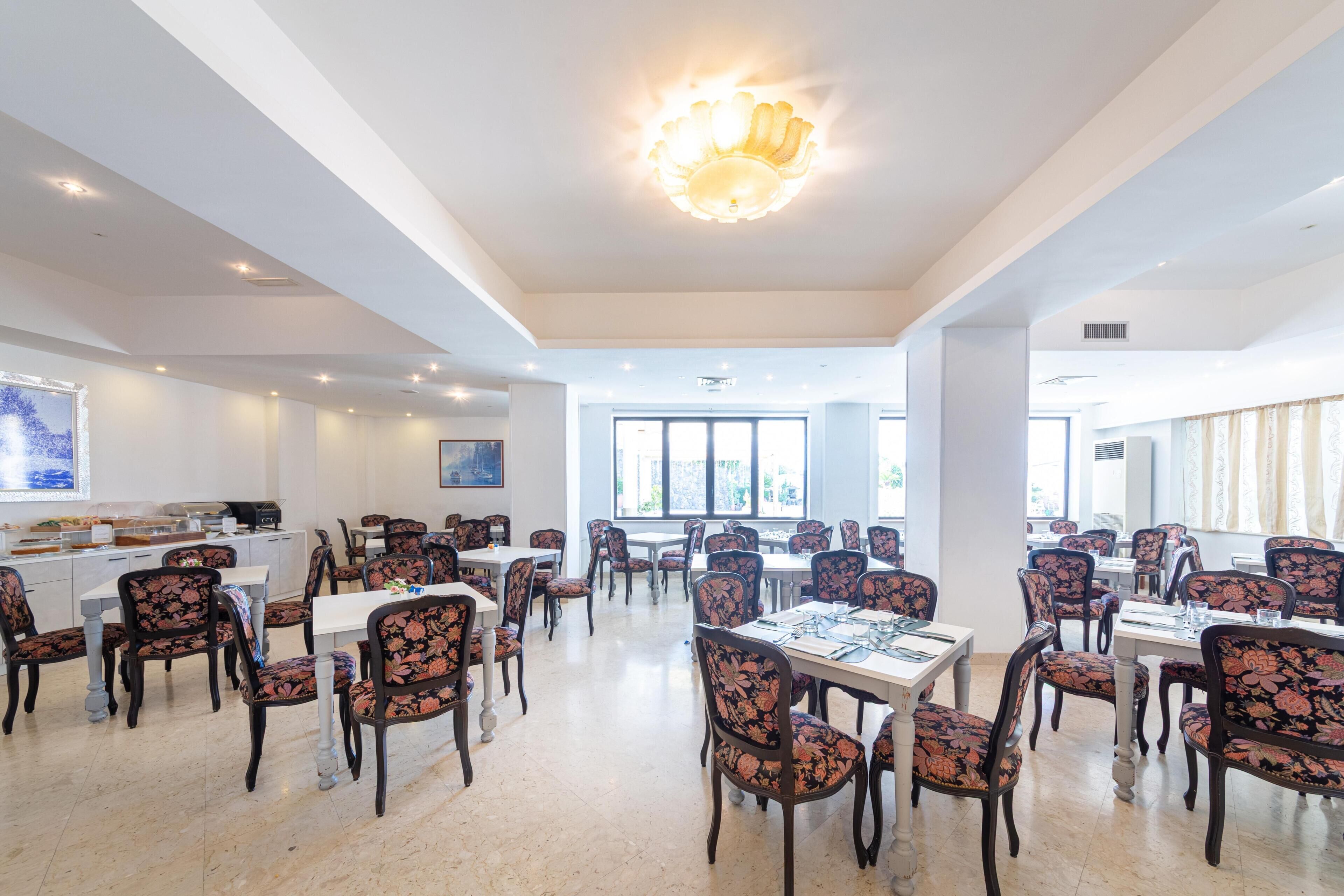 A spacious dining area with tables and chairs, a chandelier, and large windows allowing natural light.
