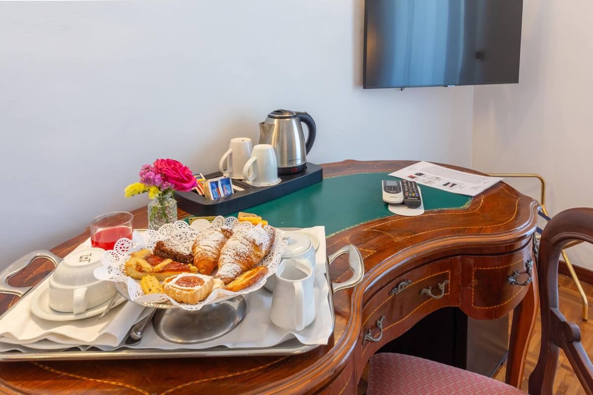 A dining table with a tray of pastries, a vase of flowers, a kettle, and a remote control.