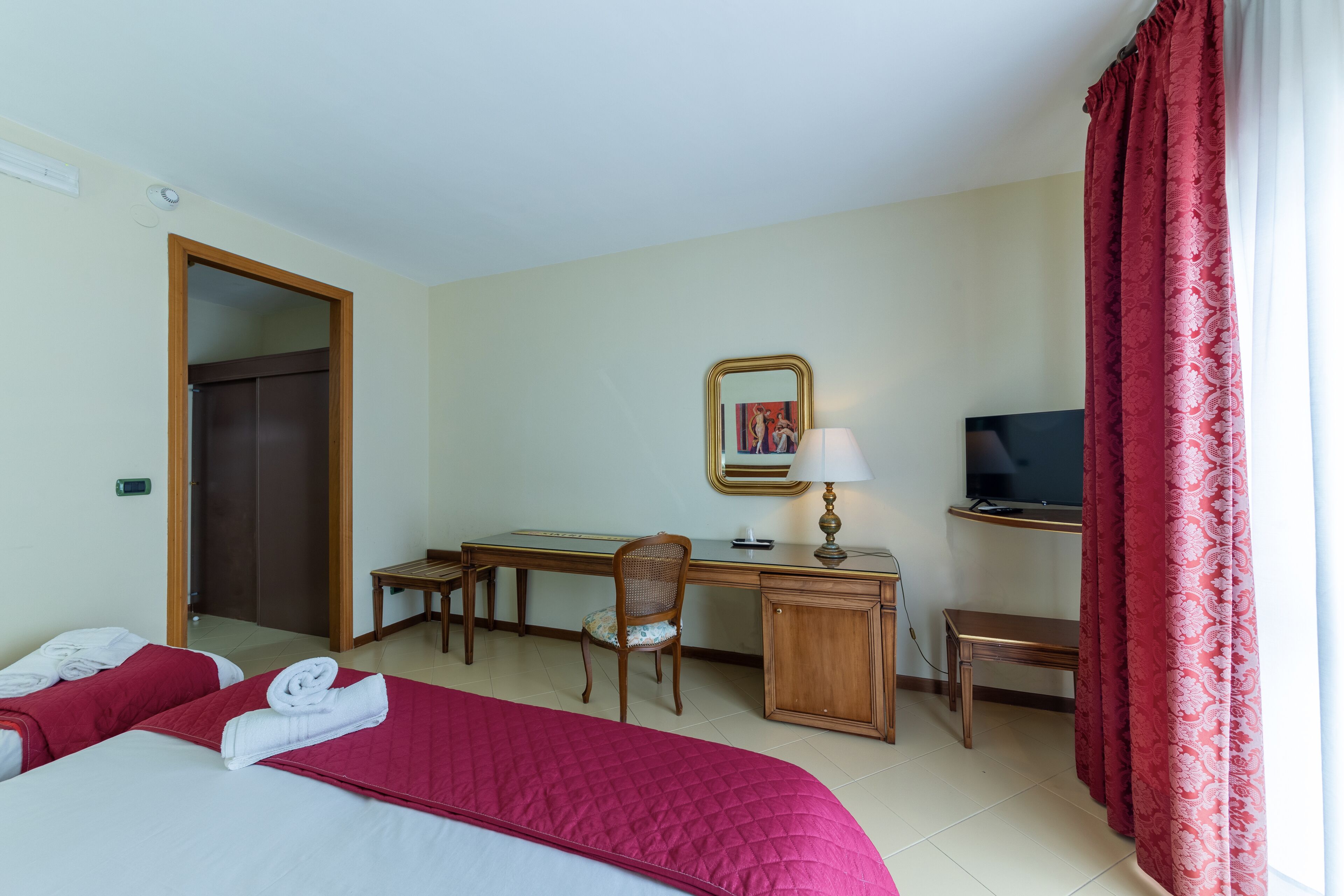 Una camera d'albergo con un letto, una scrivania, una sedia, una TV e uno specchio.