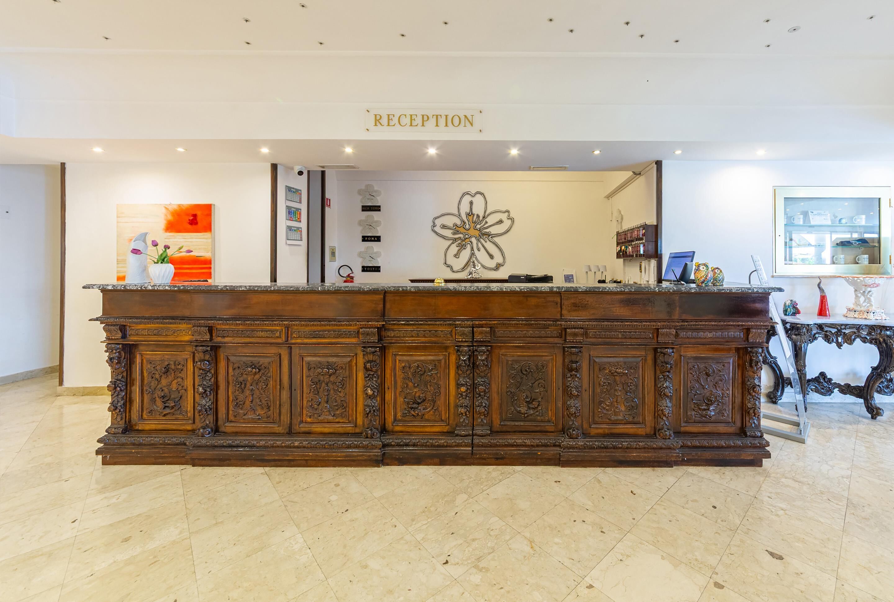 A reception desk with a 'RECEPTION' sign, a floral artwork, and a glass display case with items.