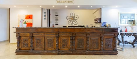 A reception desk with a 'RECEPTION' sign, a floral artwork, and a glass display case with items.