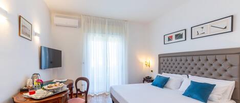A hotel room with a bed, a desk with breakfast, a TV, and artwork on the walls.