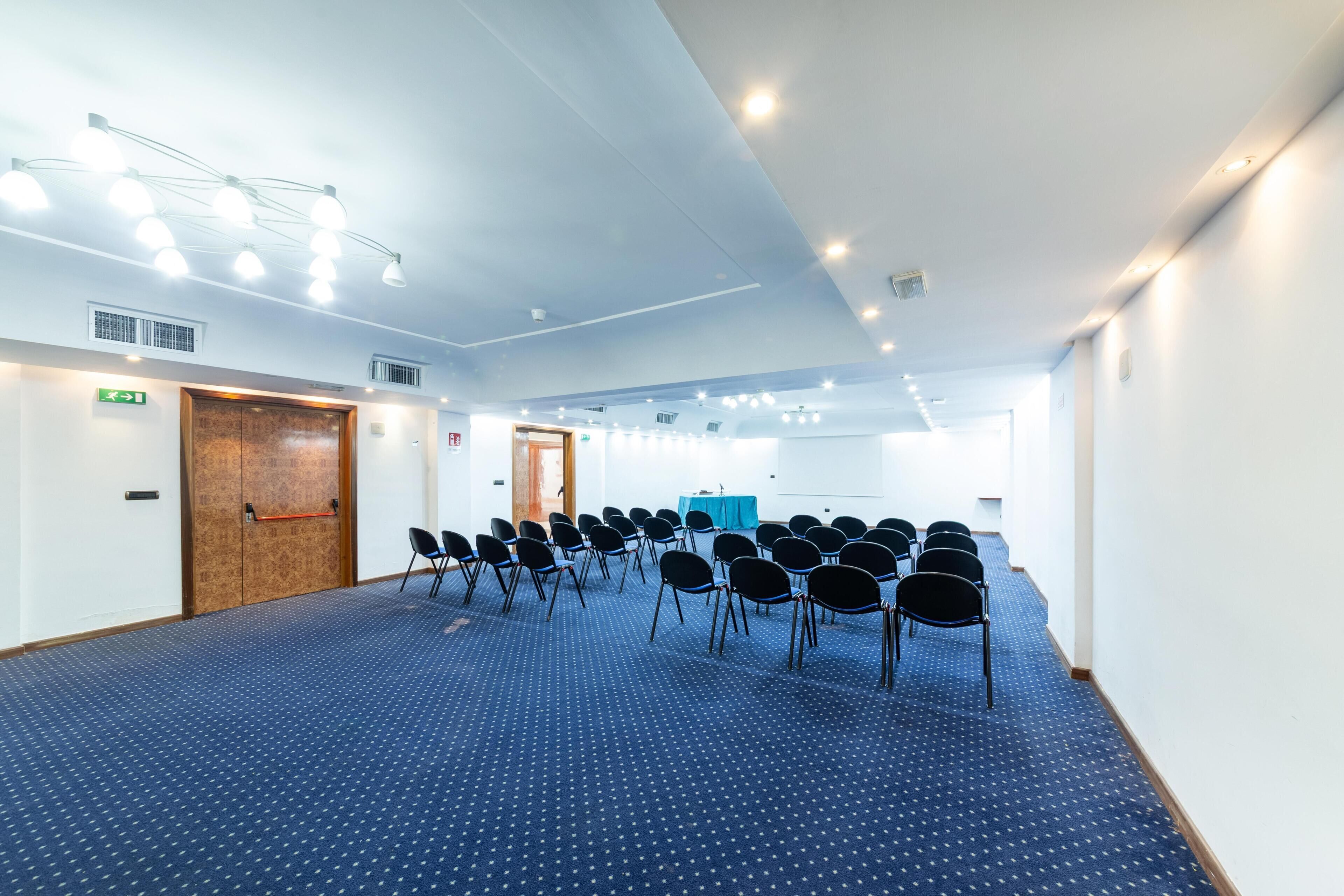 Un salón de conferencias con filas de sillas, una puerta de madera y una pizarra.