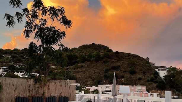 Una piscina con sillones de descanso, una cerca de madera y vistas a una colina con edificios al fondo.