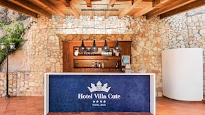 Zona de bar junto a la piscina, con un muro de piedra de fondo, vigas de madera y una barra que exhibe diferentes botellas y un televisor.