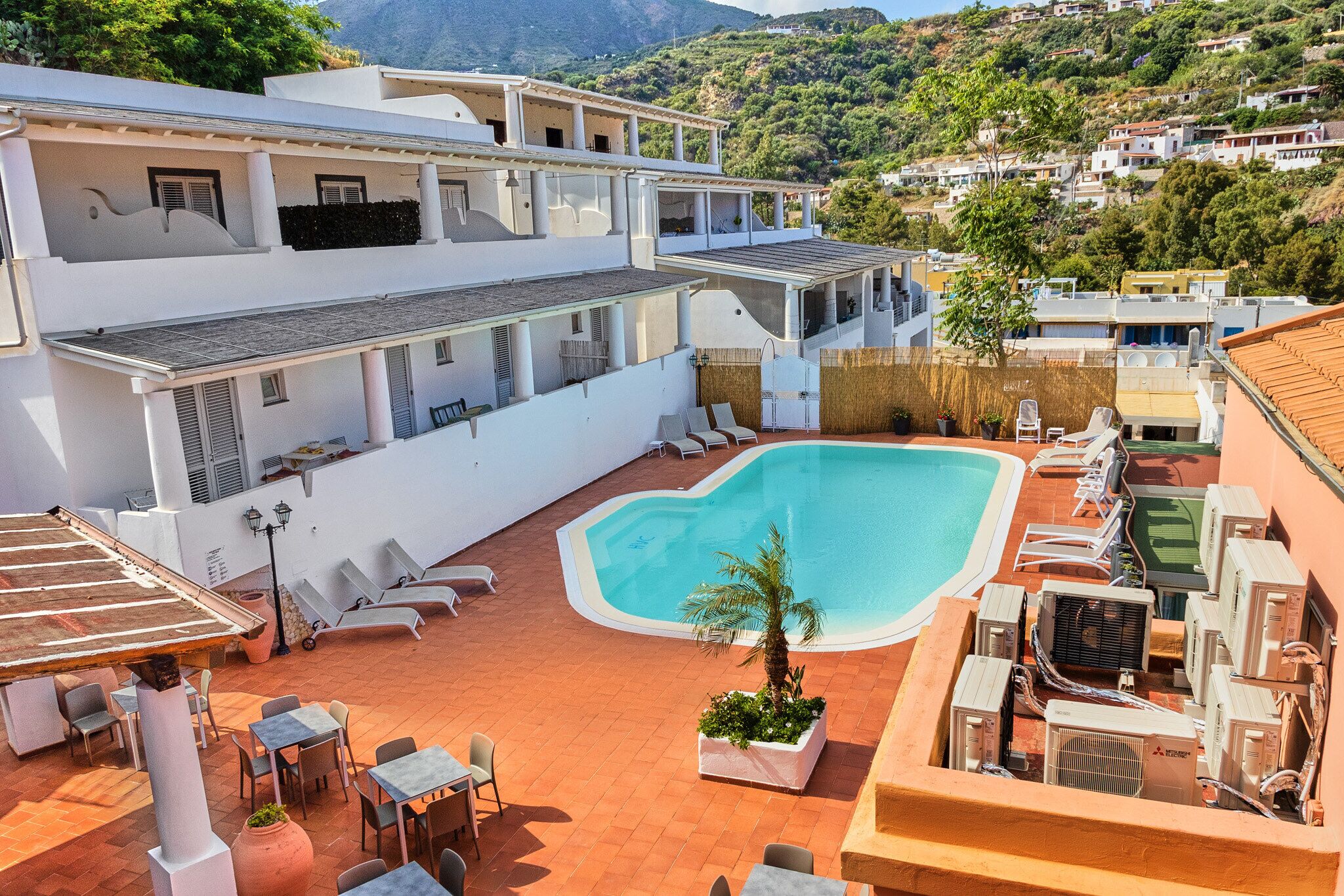 A rooftop pool area with lounge chairs, a palm tree, and air conditioning units.