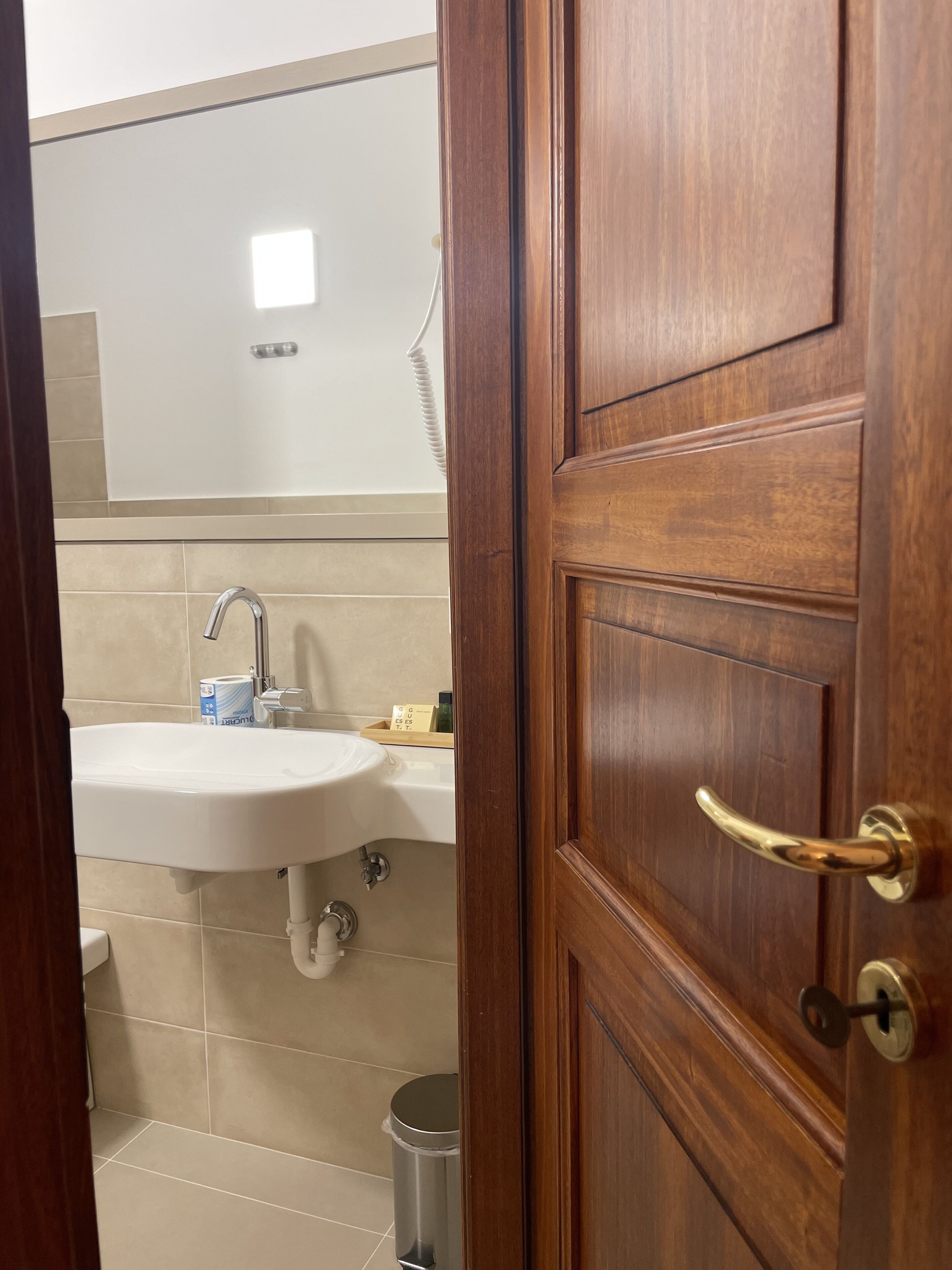 Ein Badezimmer mit einem weißen Waschbecken, einem Spiegel und einer Holztür mit Messinggriffen.