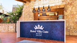 Zona de bar junto a la piscina con un fondo de pared de piedra, lámparas colgantes y una barra con bebidas embotelladas.
