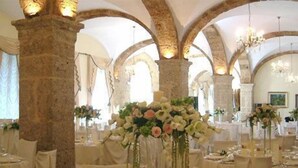 A banquet hall with stone columns, chandeliers, and tables set for a formal event.