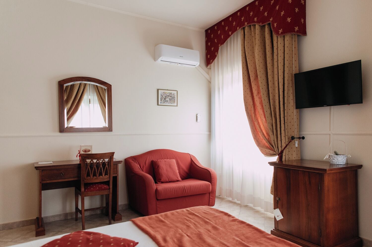 A hotel room with a bed, a desk, a chair, a TV, and curtains.