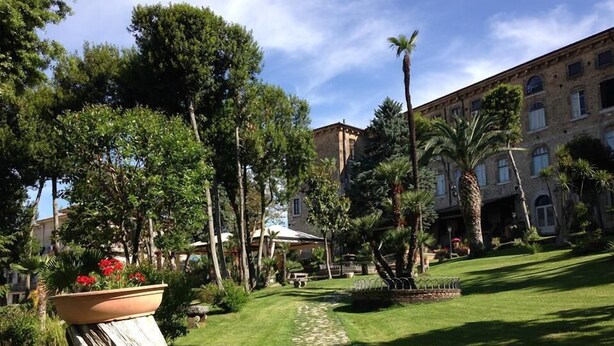 A courtyard with a stone pathway, lush greenery, palm trees, and a building with multiple windows.