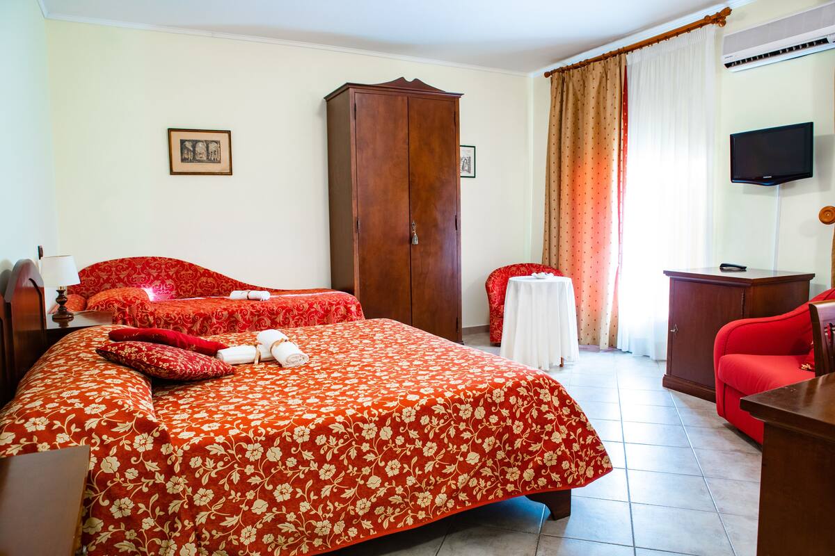 Une chambre d’hôtel avec un grand lit, une armoire, un bureau, une télévision et une fenêtre avec des rideaux.