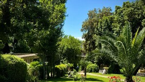 A lush garden with a stone table and chairs, surrounded by various plants and trees.