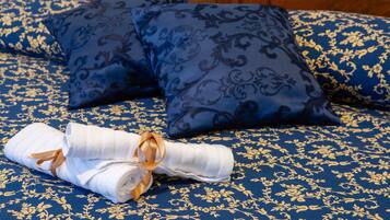 Una cama con ropa de cama de diseño azul y dorado, una toalla blanca doblada con un lazo dorado, y dos almohadas a juego.