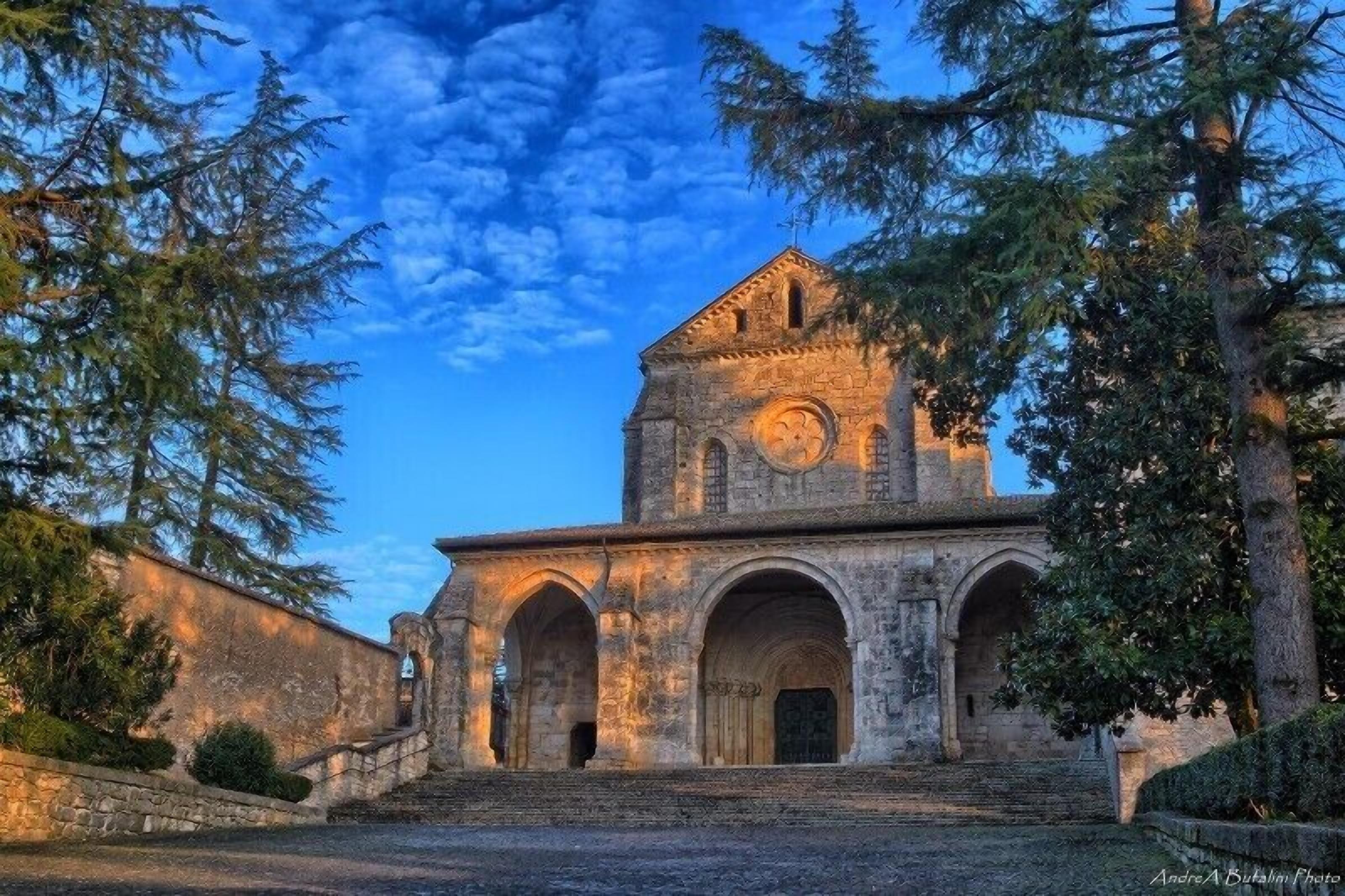 A historic stone building with a clock tower, arched entrance, and a staircase leading up to the main entrance.