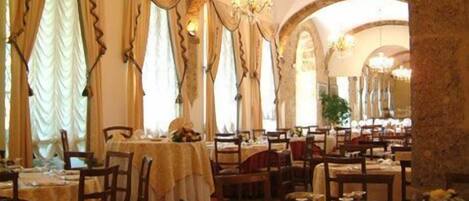 Un restaurante con varias mesas, cada una cubierta con manteles blancos y sillas, y cortinas colgantes.
