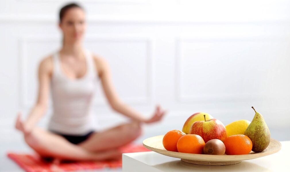 A person meditating on a red mat with a plate of fruits in the foreground.