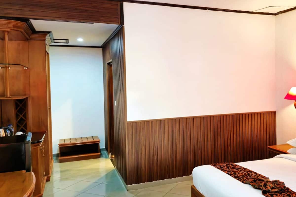 A hotel room with a bed, a wooden wardrobe, a desk, and a nightstand with a lamp.