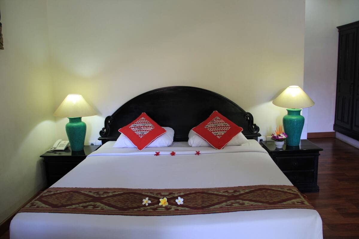 A neatly made bed with a patterned bedspread, two red decorative pillows, and two bedside lamps on black nightstands.