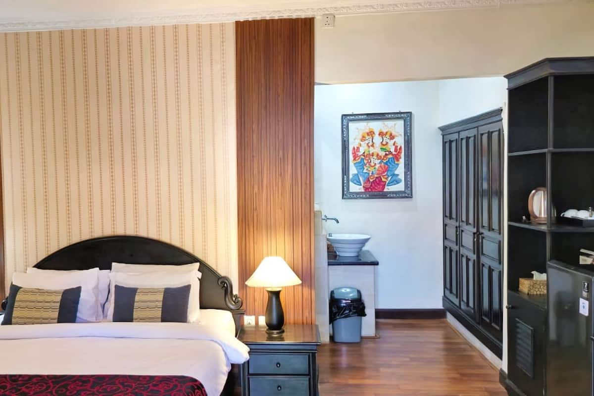 A hotel room with a bed, two bedside tables, a nightstand, a wardrobe, a sink, and a trash bin.