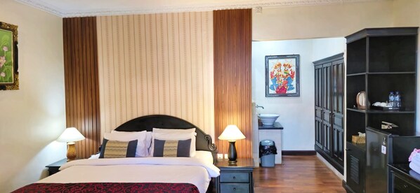 A hotel room with a bed, two bedside tables, a nightstand, a wardrobe, a sink, and a trash bin. - Stana Puri Gopa Hotel (Denpasar)