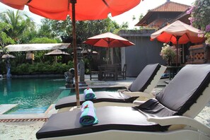 A poolside area with lounge chairs, umbrellas, and a statue. - Stana Puri Gopa Hotel (Denpasar)