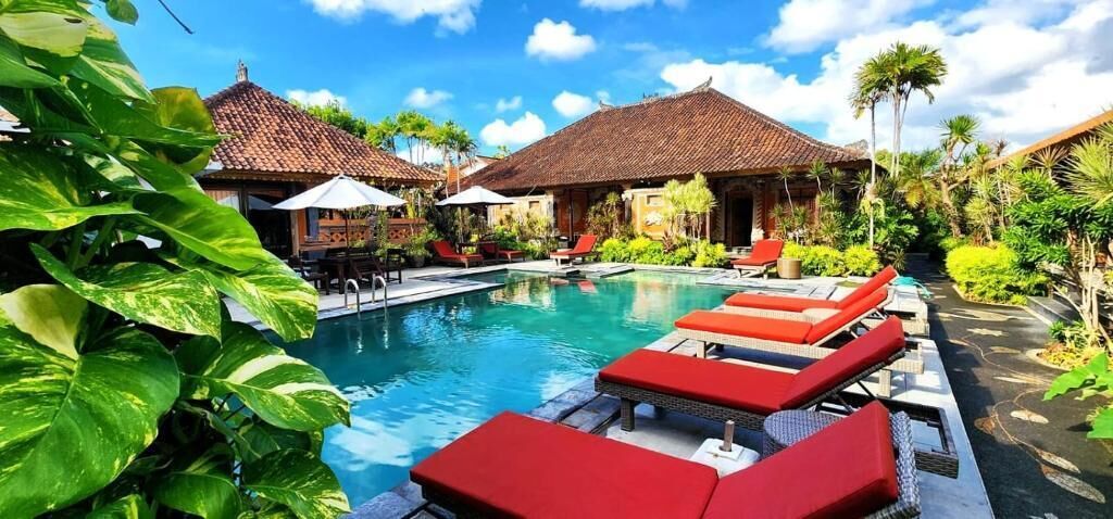 A pool area with red lounge chairs, a clear blue pool, and traditional-style buildings with tiled roofs.