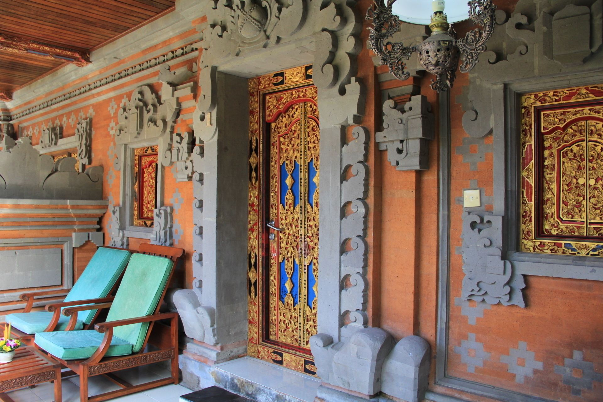 A traditional Balinese temple interior with ornate carvings, a wooden ceiling, and a bench with cushions.