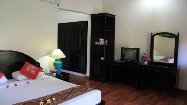 A hotel room with a bed, a desk, a wardrobe, a television, and a mirror. - Stana Puri Gopa Hotel (Denpasar)