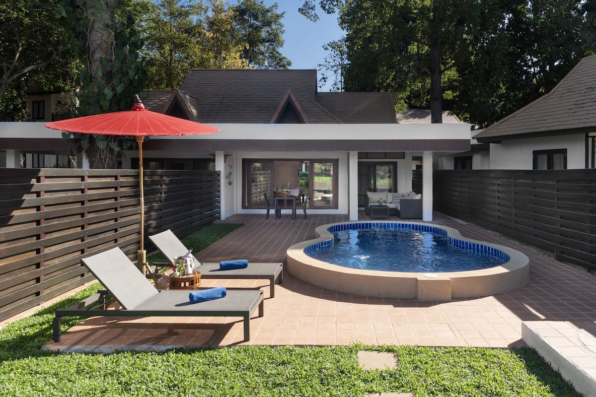 A modern house with a swimming pool, a patio with lounge chairs, and a red umbrella.