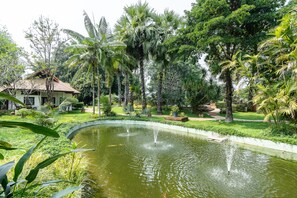 A pond with a fountain, surrounded by lush greenery and palm trees. - The Legend Chiang Rai Boutique River Resort and Spa (Chiang Rai)