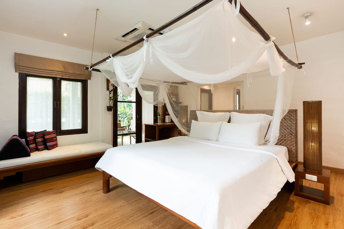 A bedroom with a four-poster bed, a bench with cushions, a bedside table, and a large window.