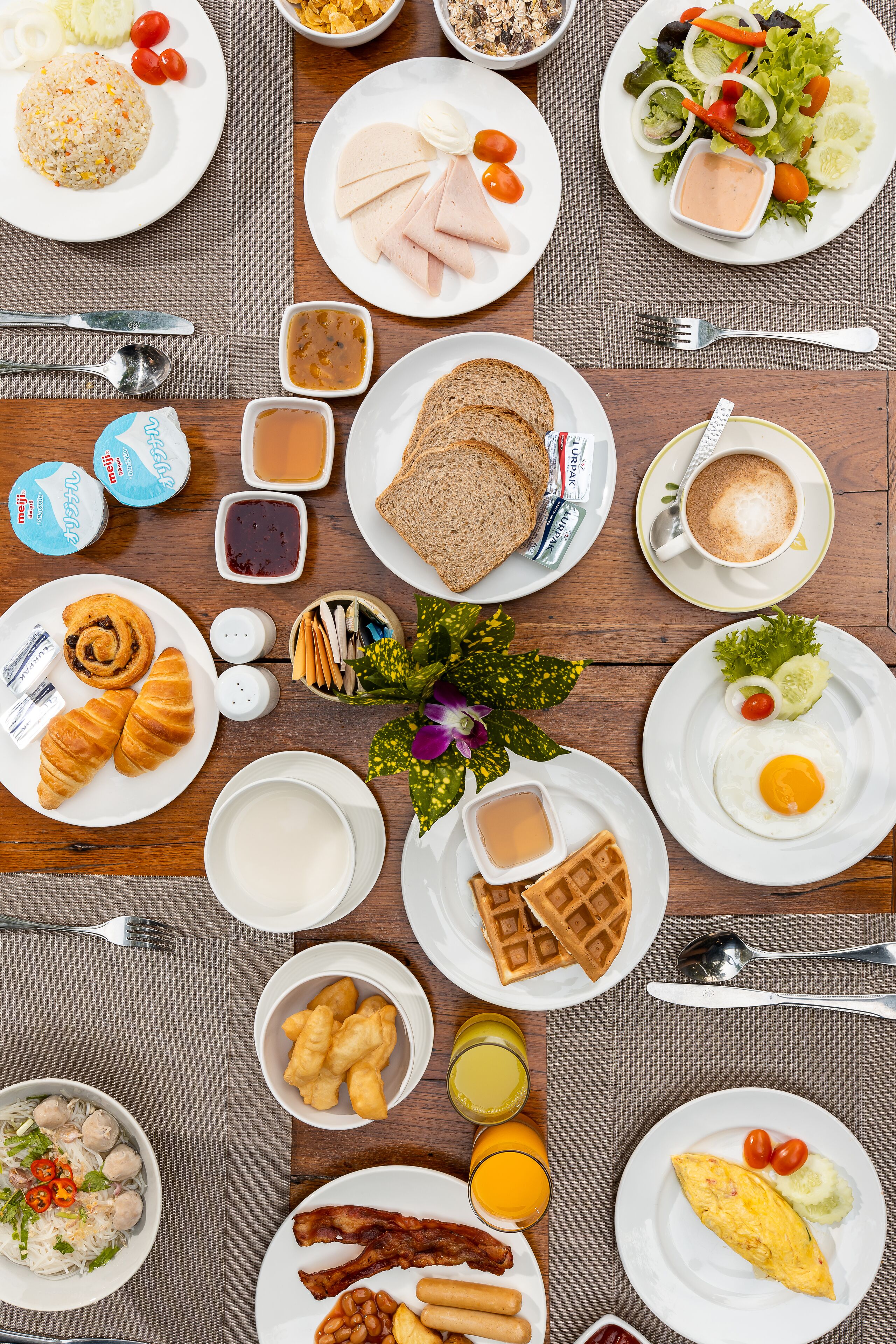Un bufé de desayuno con diversos platos, incluyendo huevos, tostadas, croissants y una ensalada.