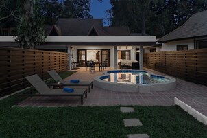 A modern house with a swimming pool, a patio with lounge chairs, and a covered outdoor dining area.