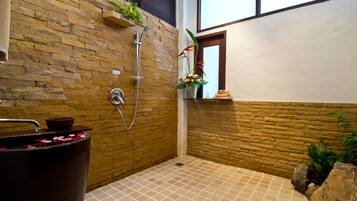 Ein Badezimmer mit einer Steinwand, einer Dusche, einer Badewanne mit Rosenblättern und einem Fenster mit Blick.