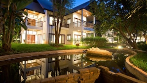 Een hotel met twee verdiepingen, balkons, een reflectie vijver en een verzorgde tuin.