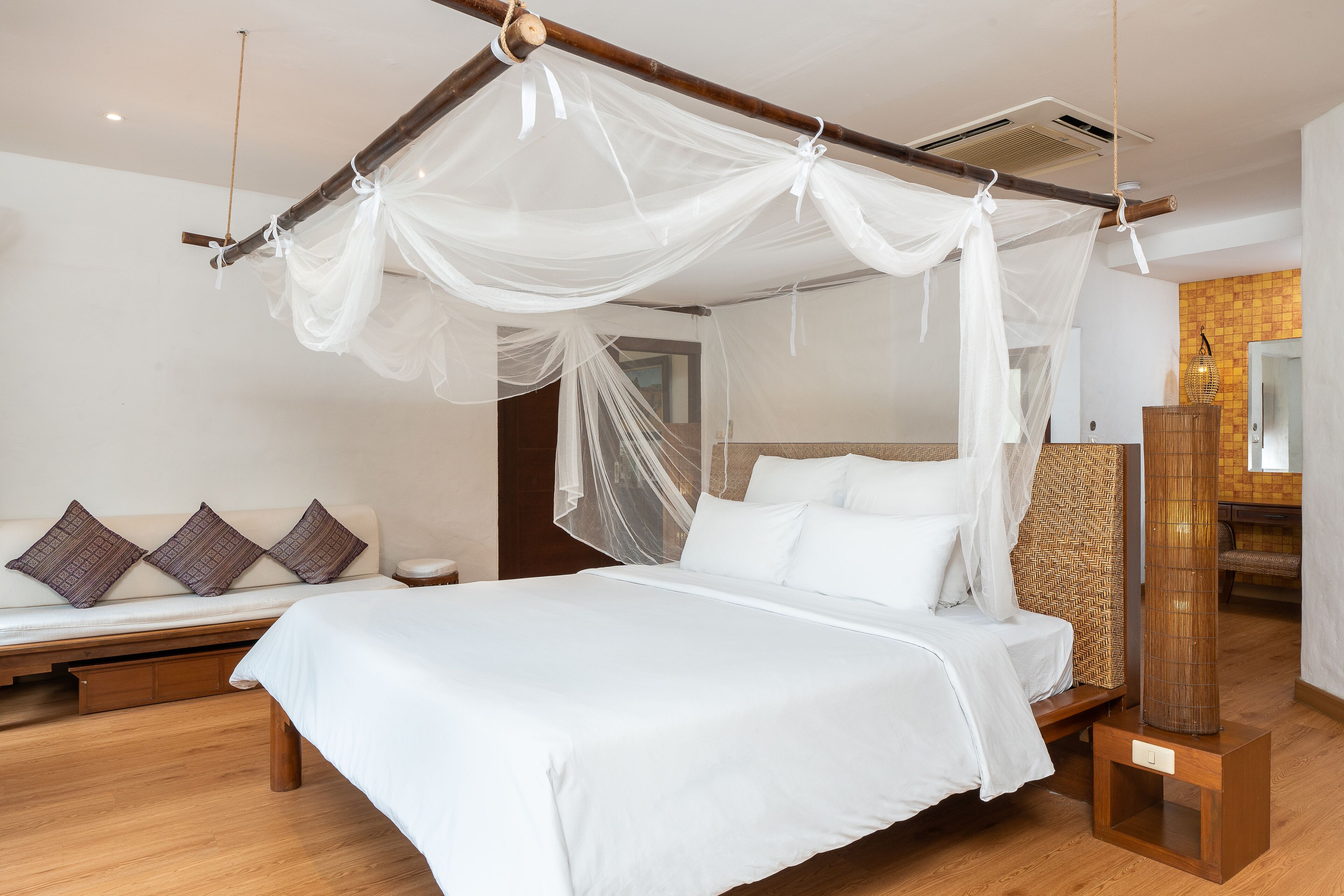 A bedroom with a four-poster bed, a bench with cushions, and a bedside table with a lamp.