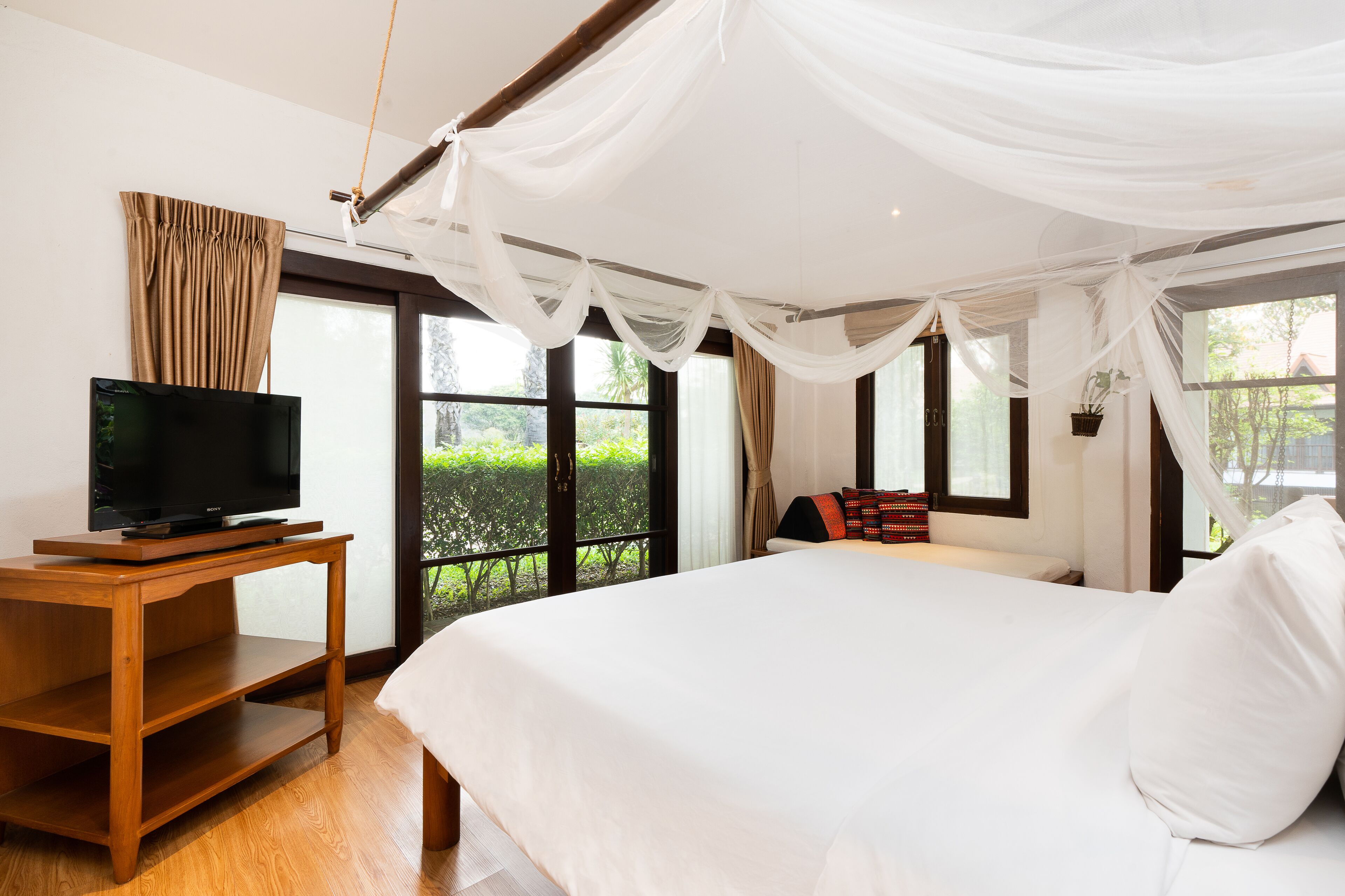 Un dormitorio con una cama grande, un televisor sobre un mueble de madera y cortinas traslúcidas.