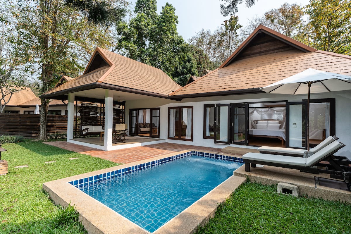 A modern house with a swimming pool, a covered patio, and a lounge area with a sun umbrella.
