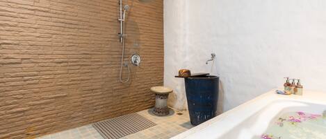 A bathroom with a stone wall, a shower, a bathtub with floral design, and a small stool.