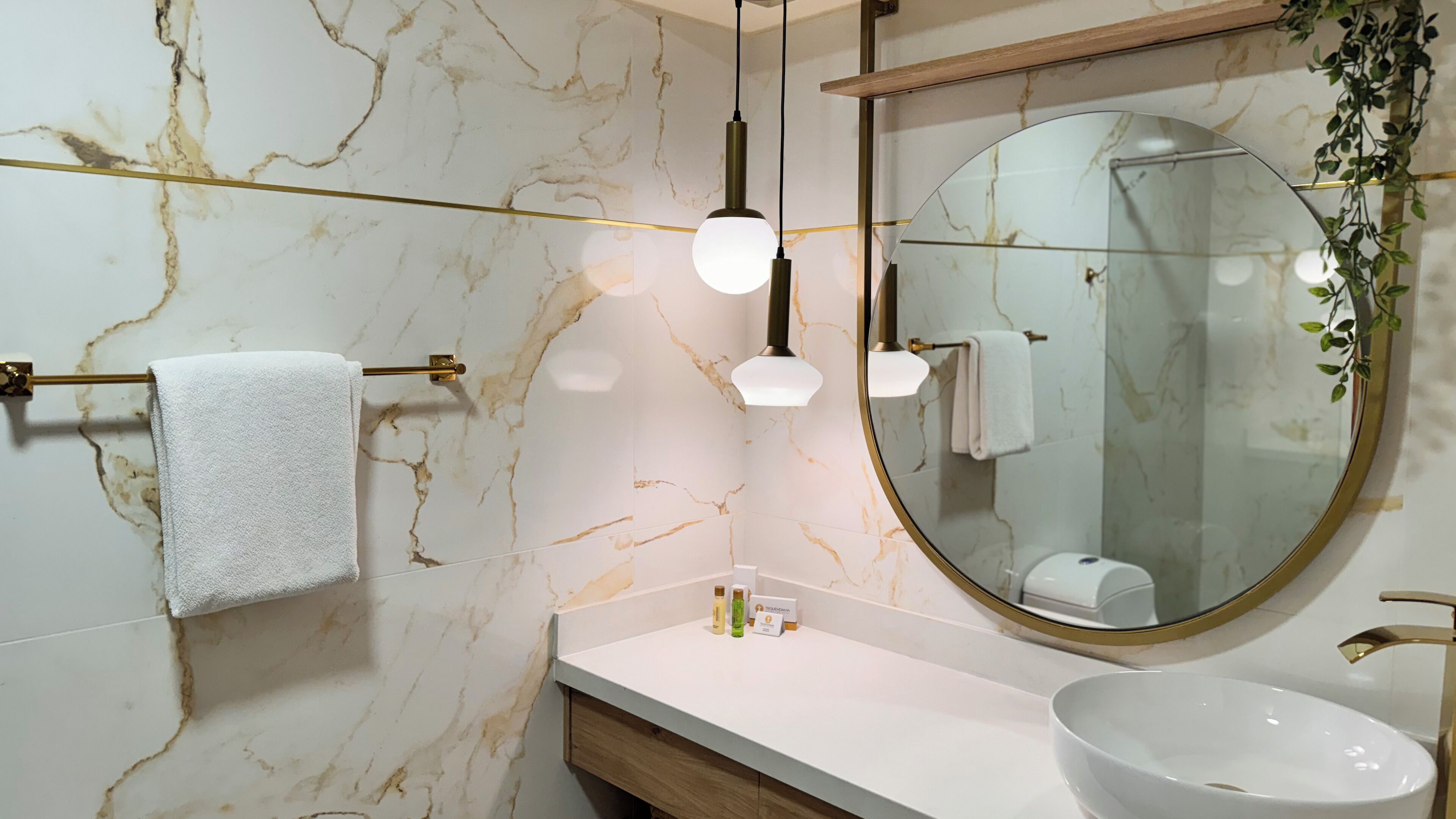 A bathroom with a marble wall, a round mirror, a white sink, and two pendant lights.