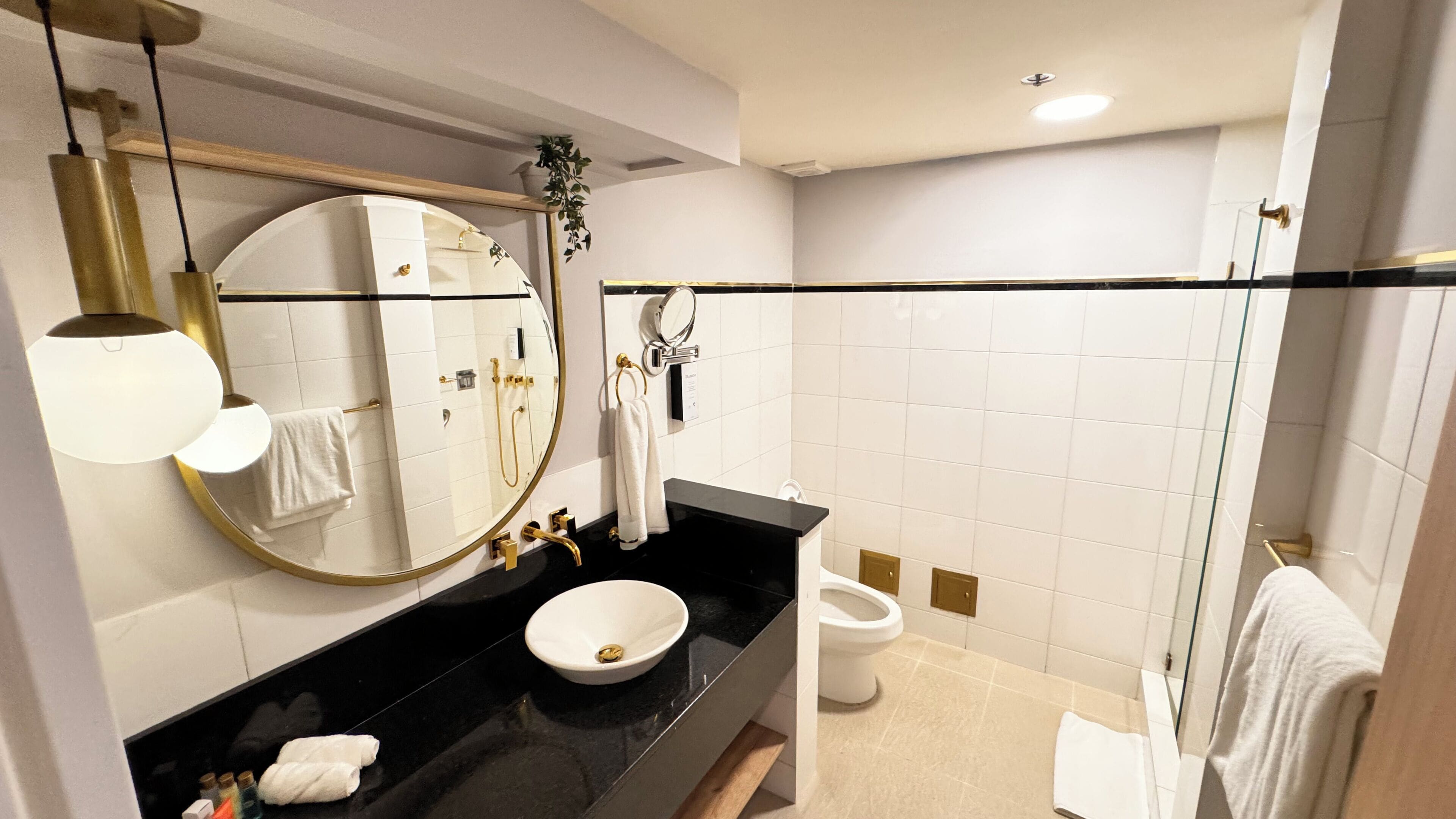 A modern bathroom with a black countertop, a round mirror, a white sink, and a glass shower enclosure.